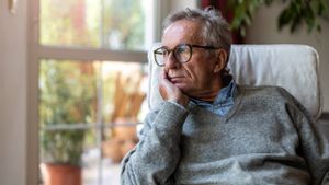 Älterer Mann mit gelangweiltem Gesichtsausdruck schaut aus einem Fenster.