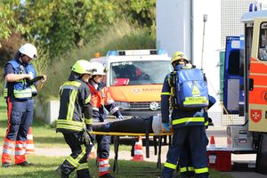 Malteser SEG-Einsatzkräfte in Einsatzkleidung versorgen eine liegende Person. Im Hintergrund: Malteser Einsatzfahrzeuge