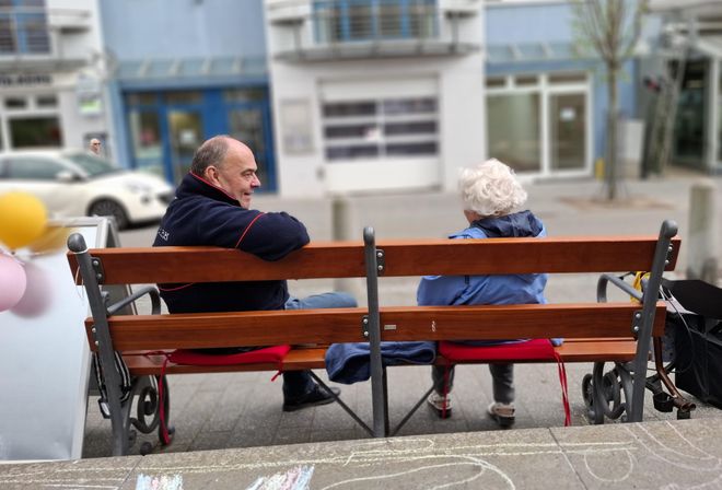 Ein Ehrenamtlicher der Malteser sitz mit einer Passantin auf einer Bank und unterhält sich