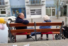 Ein Ehrenamtlicher der Malteser sitz mit einer Passantin auf einer Bank und unterhält sich