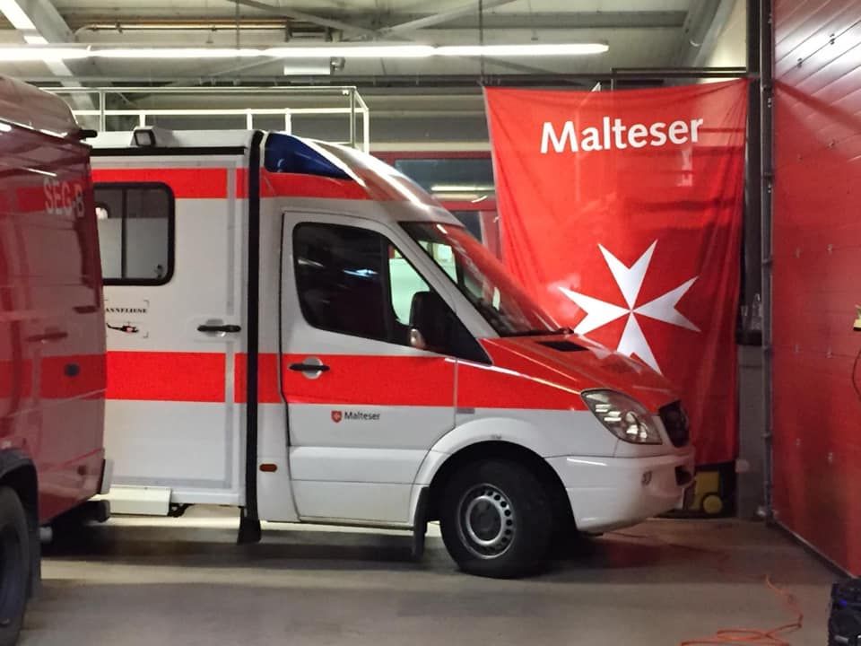 Malteser Rettungswagen steht vor der Malteser Fahne