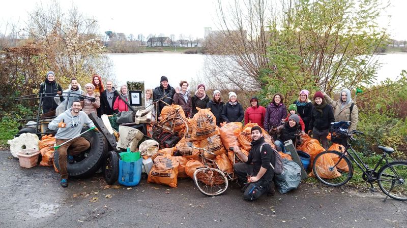 Menschen vor einem Gewässer mit orangefarbenen Müllsäcken