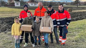 Vier Männer in Malteserkleidung stehen hinter vier Kindern und Jugendlichen, von denen zwei ein Hilfspaket in der Hand halten.