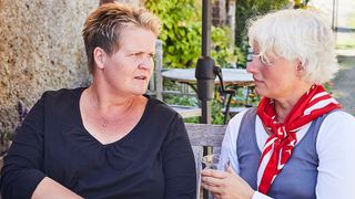 Zwei Frauen sitzen im Garten im Tisch und führen ein Gespräch. 