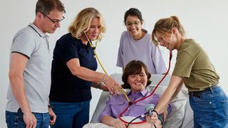 Schüler eines Ausbildungskurses üben am Krankenbett das Blutdruckmessen.