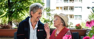 Malteser Ehrenamtliche und ältere Dame sitzen auf einem Balkon.