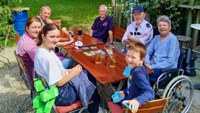 Die Familie sieht beim Herzenswunsch-Ausflug um einen Tisch: Die Frau mit ihrem Ehemann, zwei Enkel, deren Eltern und ein Malteser Helfer.. 