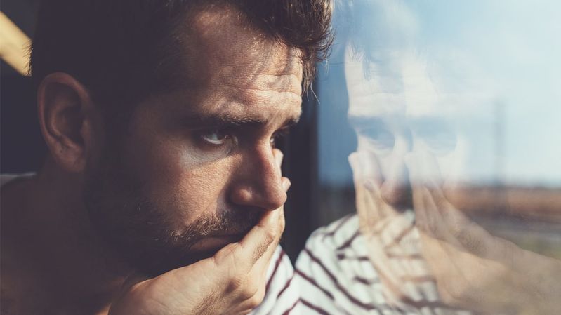 Ein junger Mann sitzt in der Bahn und schaut mit leerem Blick aus dem Fenster.