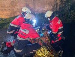 Drei Einsatzkräfte behandeln einen Verletzten, der mit einer Rettungsdecke zugedeckt ist.