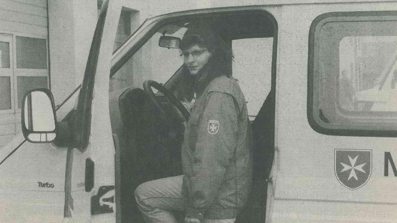 Ein monochromes Zeitungsbild einer jungen Frau mit Brille, die in ein Fahrzeug der Malteser in Deutschland steigt.