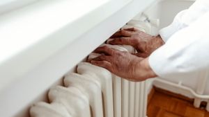 Älter aussehende Hände berühren und wärmen sich an der Heizung an.