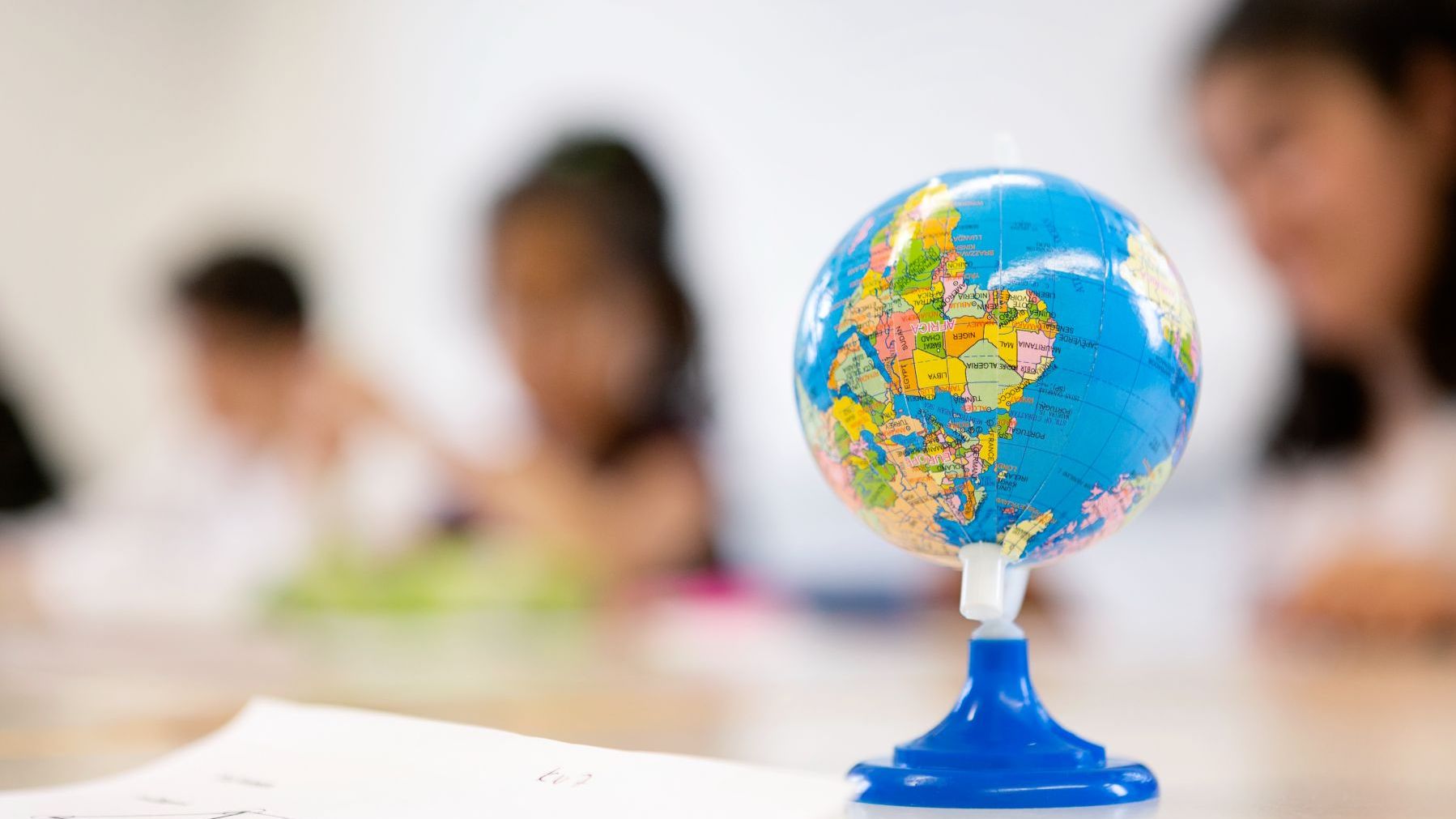 Weltkugel auf einem Tisch, im Hintergrund Kinder