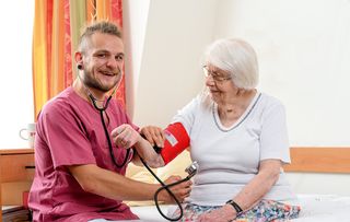 Ein Altenpfleger beim Blutdruckmessen einer älteren Dame