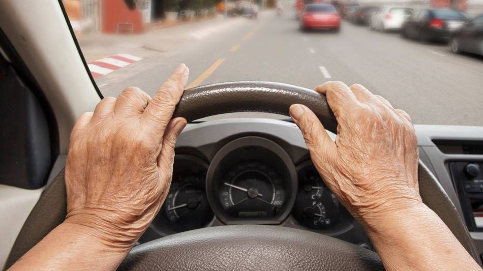 Das Auto-Lenkrad wird von einer älteren Person betätigt.