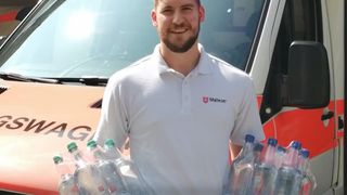 Malteser vorm Rettungswagen mit Flaschen Wasser im Arm