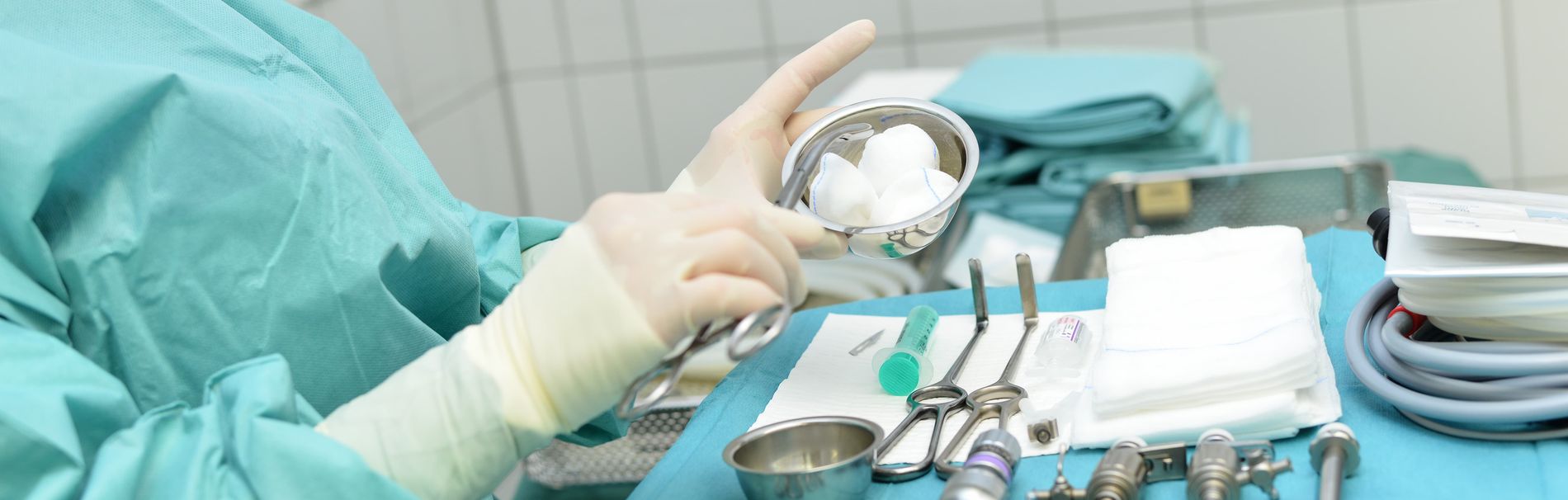 OP-Personal mit sterilen Handschuhen reicht Tupfer über vorbereitetem Operationstisch mit chirurgischen Instrumenten.