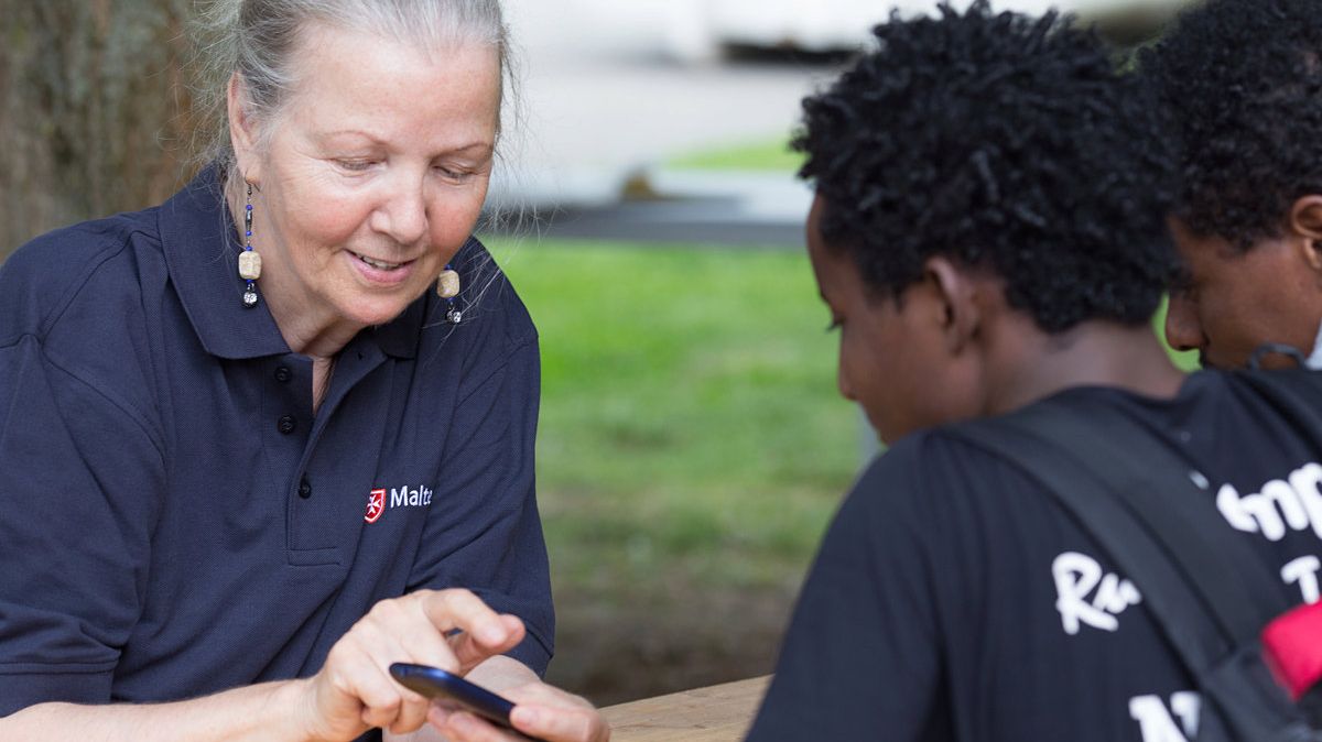 Ältere Frau zeigt jungen Flüchtlingen etwas auf dem Smartphone.