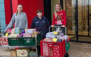 Drei Frauen mit Weihnachtsgeschenken. Die Mittlere tragt Malteser Dienstbekleidung.