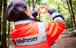 Malteser Mitarbeiterin macht mit den Fingern ein Herz