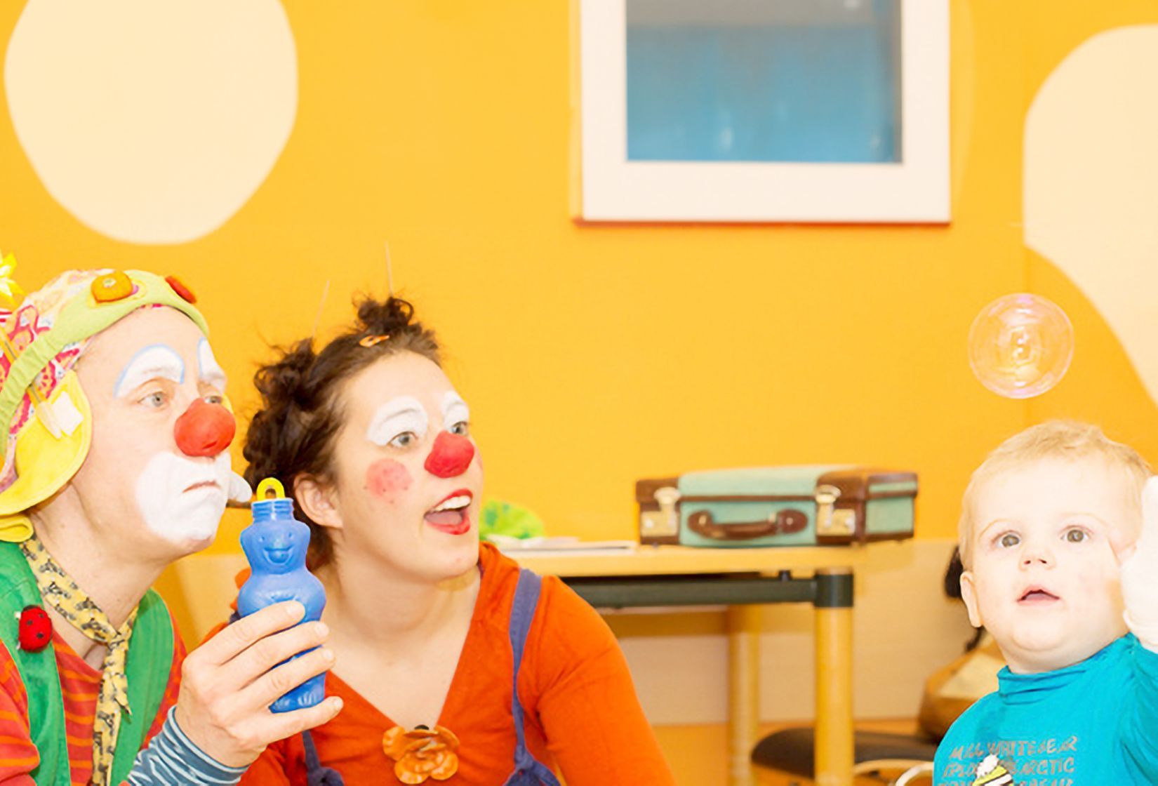 Zwei Clowns spielen mit einem kleinen Kind.