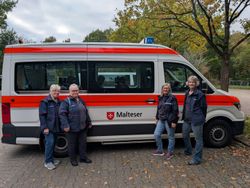 Die vier ehrenamtlichen Helferinnen des Kulturbegleitdienstes der Malteser Nordhorn posieren für ein Foto vor dem weiß-orangen Einsatzfahrzeug, das für die Touren verwendet wird.