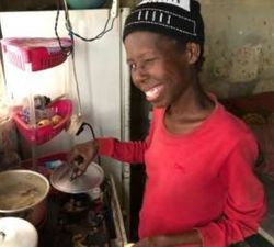A woman smiles while cooking at a stove; photograph from newsletter no. 38