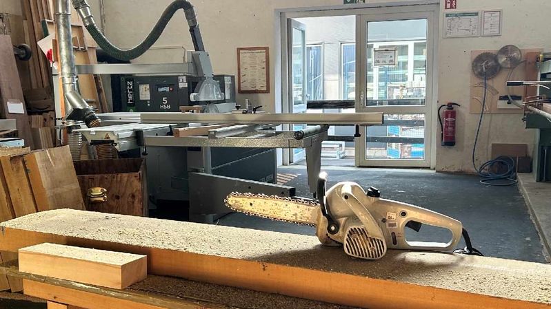 Eine Kettensäge abgelegt auf einem Holzbrett in einer Tischlerei.