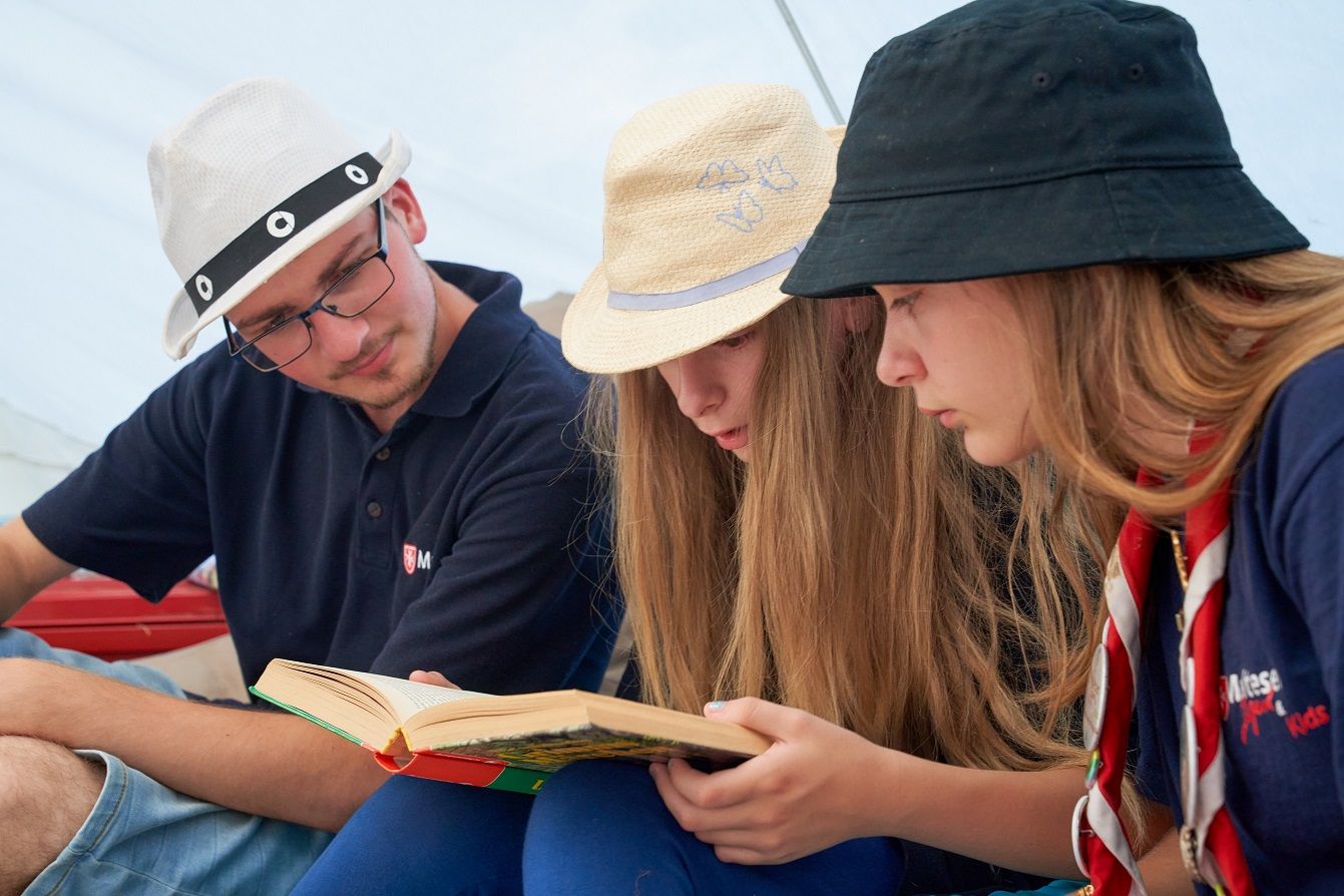 Zwei Mädchen und ein Junge sitzen zusammen und schauen in ein Buch.