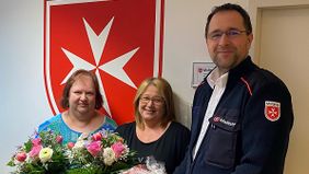 Zwei Frauen bekommen Blumen von einem Mann in Malteser-Kleidung.