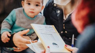 Nahaufnahme eines Untersuchungshefts für Kinder. Im Hintergrund wird ein Kind getragen.