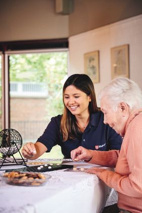 Ältere Dame sitzt am Tisch mit junger Frau und spielt ein Gesellschaftsspiel