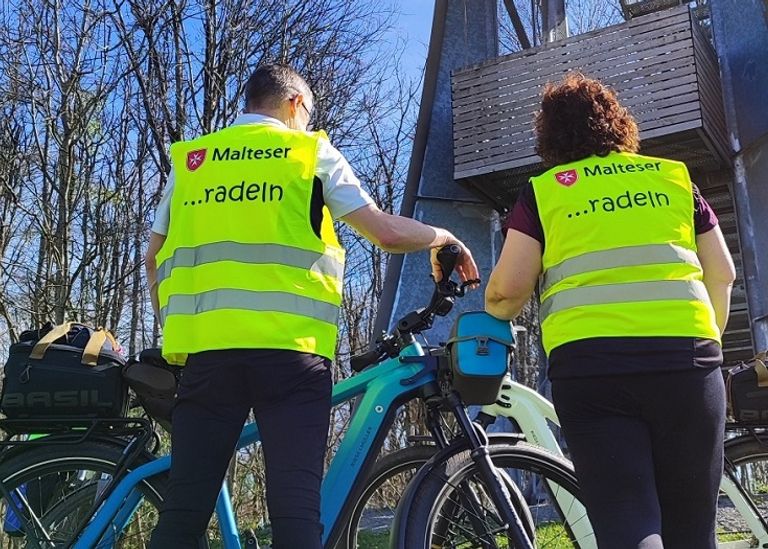Zwei Fahrradfahrer von hinten mit ihren Bike. Sie tragen eine gelbe Warnweste.