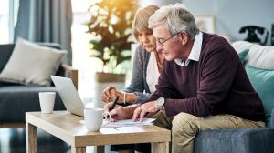 Ein älteres Paar mit Laptop und Papieren im Wohnzimmer