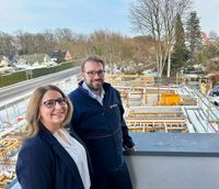 Eine Frau und ein Mann in Malteser Dienstbekleidung stehen auf einem Balkon. Im Hintergrund ist eine Baustelle zu sehen.
