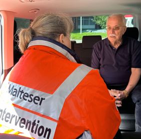 Eine Frau in Malteser Einsatzkleidung im Gespräch mit einem Mann. Beide sitzen in einem Malteser Einsatzfahrzeug.