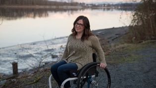 Eine Frau im Rollstuhl fährt an einem Fluss entlang.