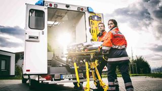 Malteser Rettungsdienstmitarbeitende verladen Krankenliege in Rettungswagen.