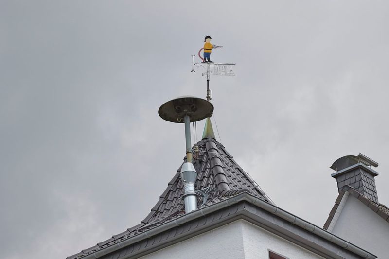 Sirene auf einem Hausdach neben einer Wetterfahne 