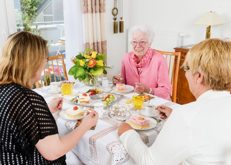 Drei Frauen sitzen an einem Tisch und essen Kuchen bei einer Kaffeerunde.