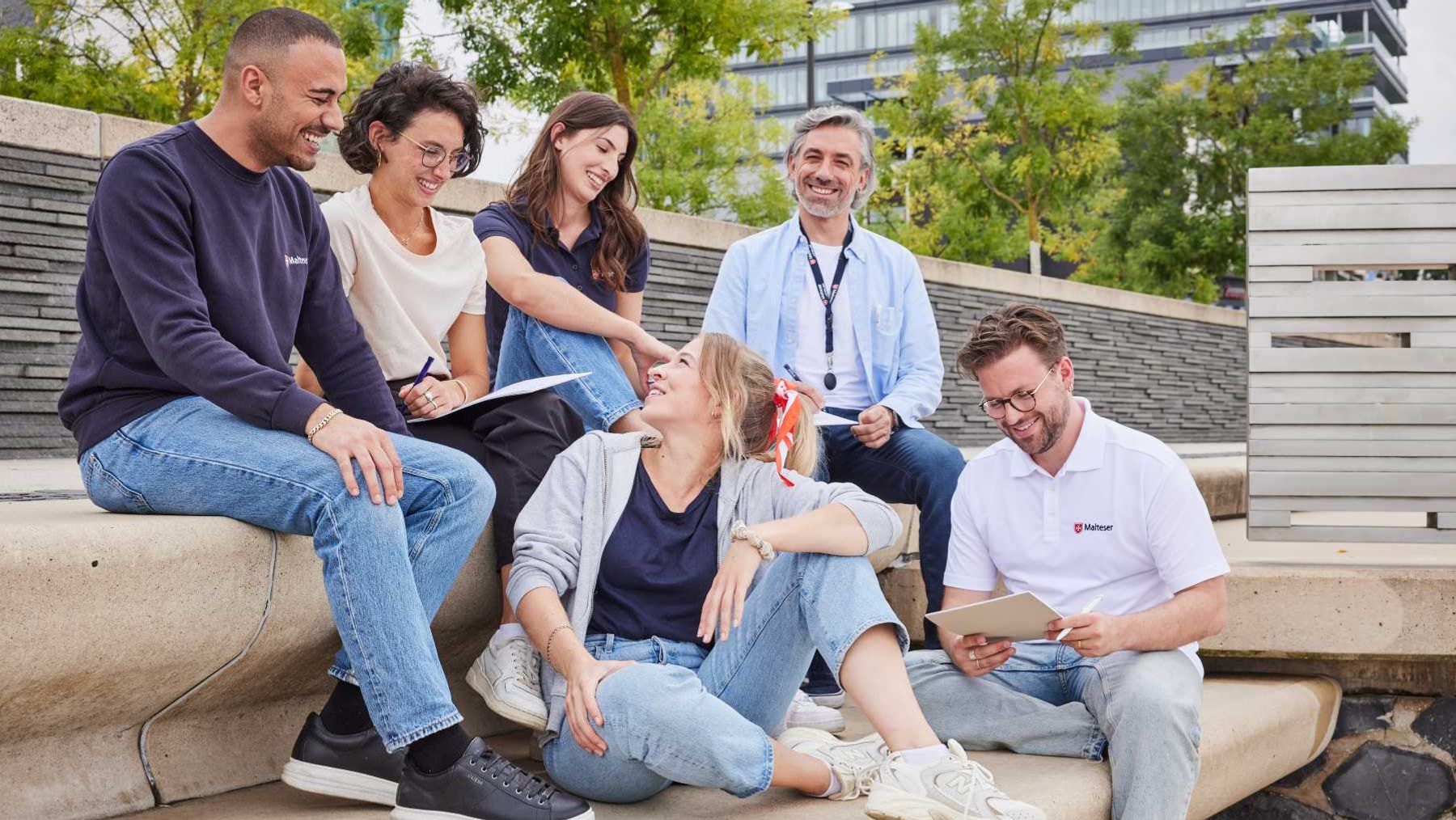 Diverse Gruppe Malteser sitzt auf einer Treppe