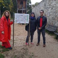 Zwei Frauen und ein Mann stehen neben einer Kommunikationstafel auf einem Spielplatz