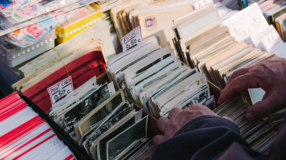: Die Hände eines älteren Mannes über alten Fotos und Postkarten an einem Flohmarktstand