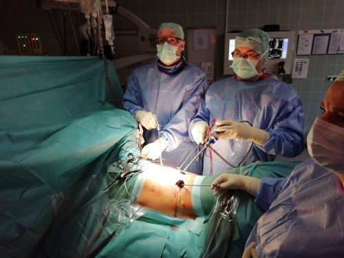 Operationsteam in steriler Kleidung führt im OP-Saal eine minimalinvasive Rückenoperation mit Kamera und Instrumenten durch.