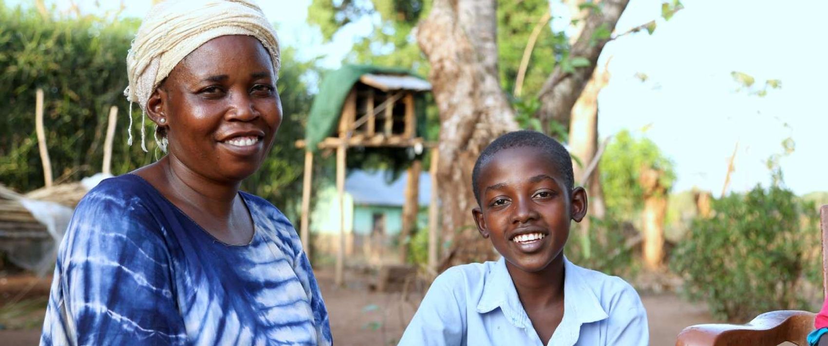 In einem Schulgarten im Südsudan sitzen eine Frau und ein Junge und lächeln in die Kamera
