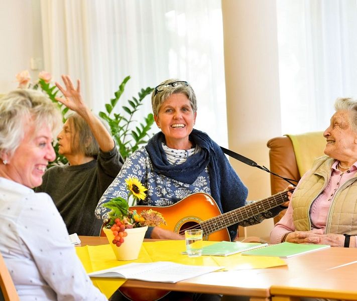 die Tagespflege spielt den Bewohner ein Lied mit einer Gitarre vor 