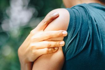 Eine Person fasst sich mit der Hand an den Oberarm.