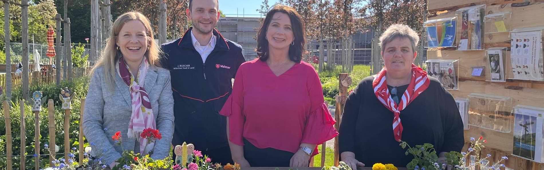 Lächelnde Menschen vor einem Hochbeet mit verschiedenen Blumen.