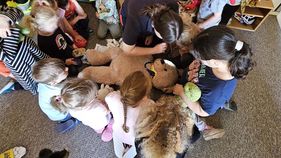 Kinder sitzen um einen Teddy, der mit einem Stethoskop abgehört wird