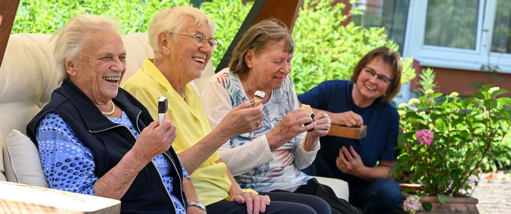 Ältere Frauen sitzen im Garten, essen Eis und lachen. 