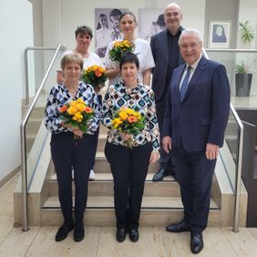 Gruppenfoto auf einer Treppe mehrere Personen halten Blumensträuße ein Mann steht vorn im Anzug.